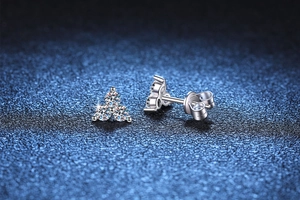 Macro shot of silver three-stone cluster earrings with sparkling moissanite on blue background