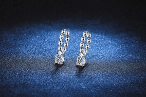 Close-up of moissanite drop earrings with beaded silver hoop on blue textured fabric