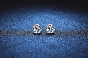 Macro shot of 925 silver six-prong moissanite stud earrings on a dark blue background