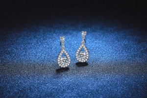 Close-up of teardrop silver earrings featuring a halo pavé setting and a moissanite stone