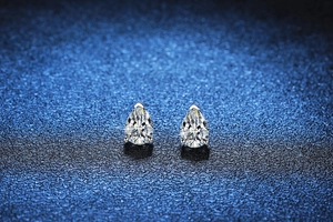 Detail of pear-cut moissanite earrings with 3-prong silver setting on dark blue base