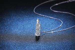 Macro shot of silver three-stone moissanite pendant on a dark blue textured backdrop