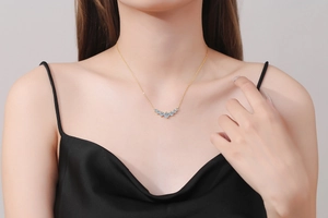 Close-up of gold smile necklace with seven blue moissanite stones on a female model