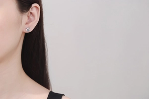 Detailed view of silver bow earrings with sparkling light blue moissanite on model