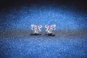 Macro view of S925 silver bow earrings with pink gemstone and round moissanite drop