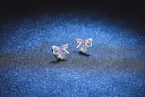 Macro shot of silver bow earrings with pink stones and sparkling round moissanite