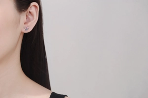 Detail of S925 silver bow stud earrings featuring light blue moissanite on a model