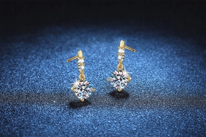 Close-up of golden drop earrings featuring shimmering moissanite stones on a blue background