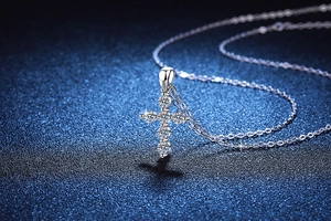 Macro shot of 925 silver cross necklace with six round moissanite stones on blue background