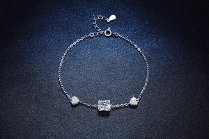 Detailed close-up of a square-cut moissanite stone and pave heart charms on silver bracelet