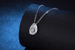 Detailed view of teardrop Moissanite pendant with three stone setting on a black stand