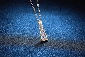 Macro shot of three round moissanite stones vertically set in a rose gold pendant necklace