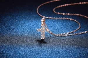 Macro shot of rose gold cross pendant with brilliant round moissanite on dark blue base
