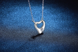 Macro shot of silver S925 heart pendant with a sparkling moissanite stone on a blue surface