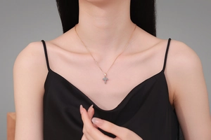 Detailed view of a gold cross pendant necklace inlaid with blue moissanite stones on a model