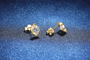 Macro shot of gold swirl stud earrings featuring 1 carat round cut moissanite stones