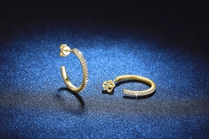 Close-up of gold C-shaped hoop earrings with pavé set crystals on a navy background
