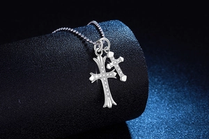 Détail de deux pendentifs en croix avec pavé de pierres brillantes sur chaîne à perles