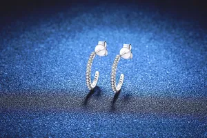 Macro shot of 925 sterling silver C-shaped earrings with zircon inlay on blue background