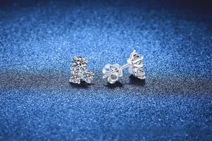 Macro detail of S925 sterling silver three-stone moissanite earrings on a blue background