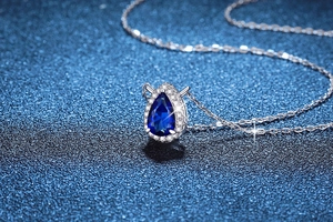 Macro shot of a pear-cut blue sapphire pendant necklace with halo zircons in silver