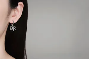 Detail of silver five-petal flower earring with light blue stone on model ear