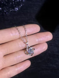 Macro view of a clover-shaped silver pendant with a large moissanite center stone and crystals