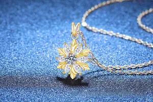 Detailed close-up of a golden snowflake pendant with zircon stones on a blue background
