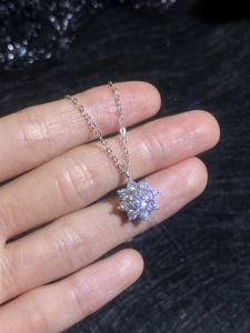 Detailed view of sunflower Moissanite pendant necklace held in hand on dark fabric