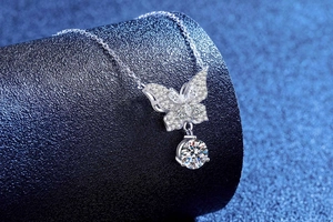 Macro detail of silver bow pendant necklace with sparkling zircons on blue texture