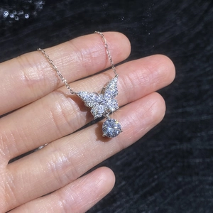 S925 silver bow necklace with moissanite pendant held against a black texture