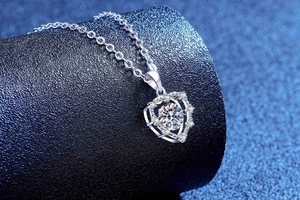 Macro shot of silver heart pendant with sparkling moissanite center on a black jewelry stand