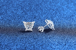 Detailed view of silver butterfly stud earrings with sparkling moissanite on a blue background