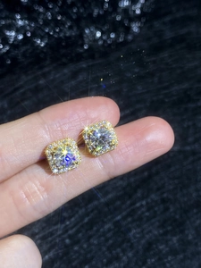 Vue macro de boucles d'oreilles moissanite carrées dorées tenues à la main par le doigt