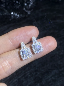Detailed view of square halo moissanite stud earrings held by hand on black texture