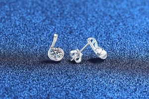 Macro shot of silver note-shaped moissanite studs with butterfly backs on blue background