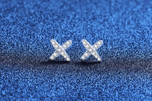 Detailed view of silver X-shaped earrings with sparkling cubic zirconia on starry background
