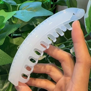 Détail d'une pince banane blanc translucide mate tenue devant des feuilles vertes