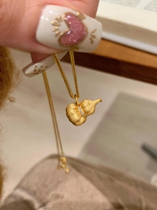Macro detail of brushed gold pumpkin gourd pendant necklace with zircon inlay on hand