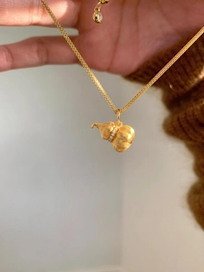 Close-up of golden Wulu pumpkin necklace pendant with brushed metal texture and tiny diamonds