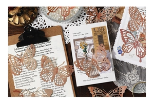 Detailed view of rose gold cutout butterfly charms with pearls for DIY vintage scrapbooking