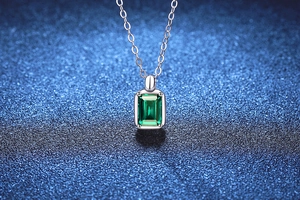 Dettaglio di un ciondolo con smeraldo su una catena in argento S925 su sfondo blu scuro