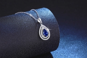 Detailed close-up of water drop pear-shaped blue sapphire pendant with double diamond halo