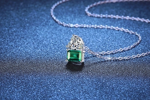 Detail of emerald necklace with heart moissanite pendant on elegant blue background
