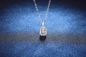 Macro-opname van een zilveren ketting met rechthoekige smaragd hanger op blauwe achtergrond