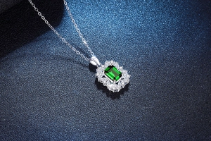 Close-up of emerald cut green gemstone pendant with marquise halo on silver chain