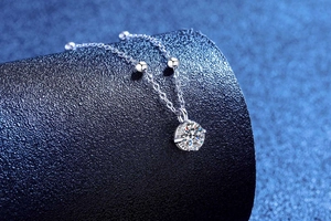 Macro shot of silver moissanite pendant with four-prong setting and beaded chain detail