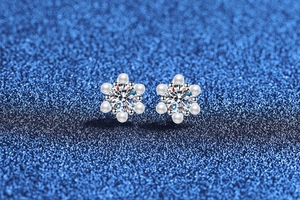 Macro detail of snowflake earrings with moissanite center and pearl petals on blue background