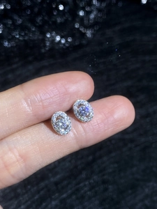 Macro view of S925 sterling silver oval halo moissanite stud earrings on fingers