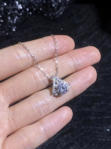 Close-up of sparkling moissanite fan pendant necklace held in hand against dark backdrop